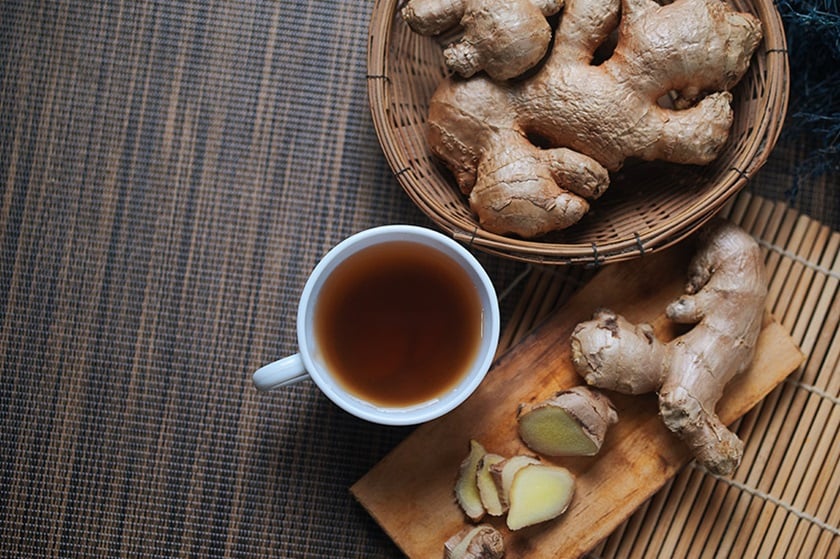 A cup of ginger tea with ginger roots next to it.