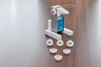 Sterillium disinfectant in a dispenser stands on a table. In front of it are 5 sensors from the NosoEX system