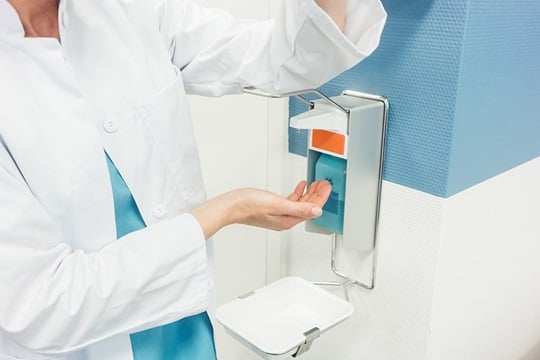 A doctor disinfects her hands at a disinfectant dispenser.