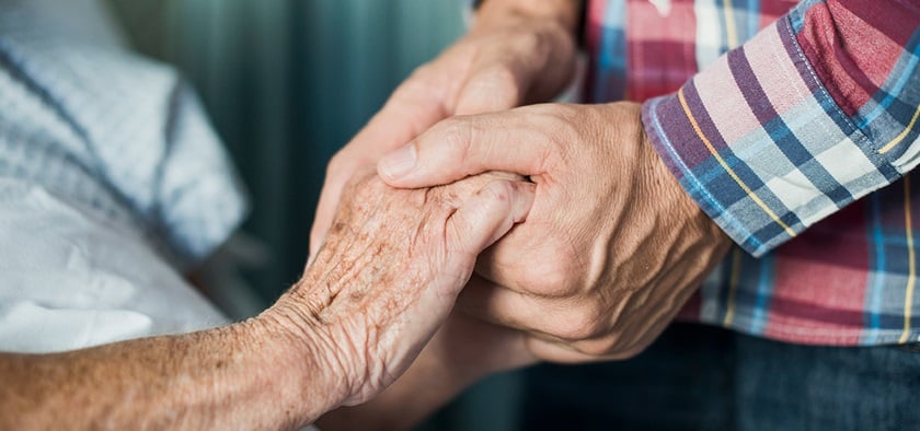 The hands of a man clasp the hands of an older person.