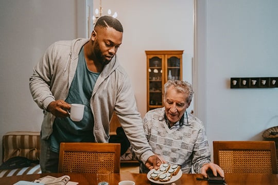A young man hands a plate of sandwiches to an older man at the dining table.