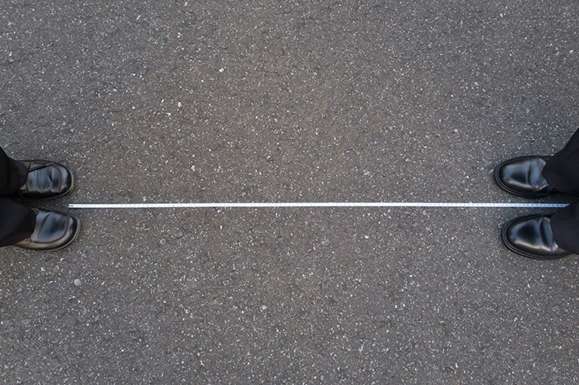 Two people stand opposite each other, a white line indicates the distance they must keep.