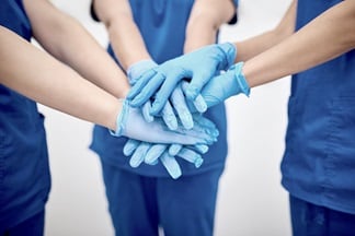 Hospital staff wearing medical gloves stand in semicircle and stack hands