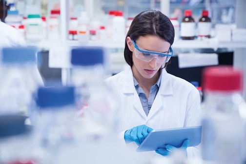 Woman with safety goggles in a lab looks into a tablet