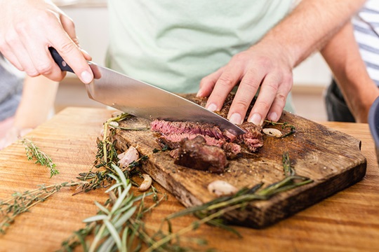 Photo of a wooden board and someone cutting meat. 