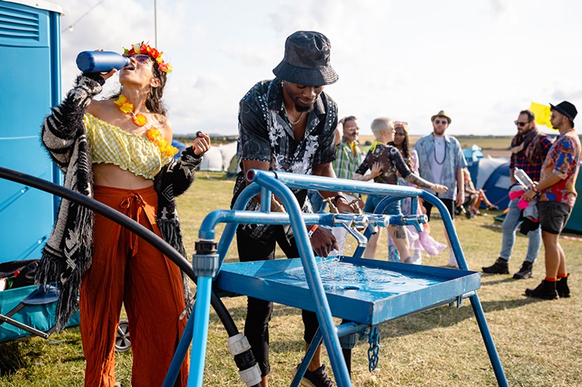 A man and a woman at a mobile water dispenser at a festival.