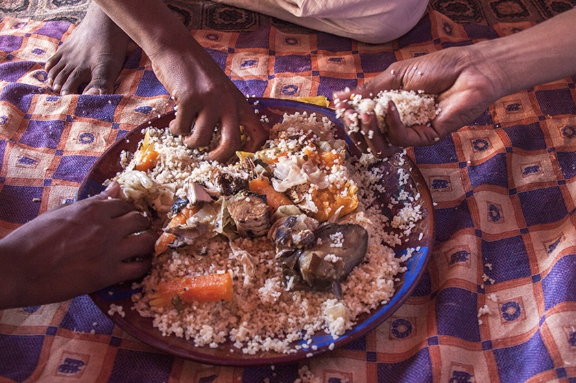 Several people eat with their hands from a bowl of rice and vegetables.