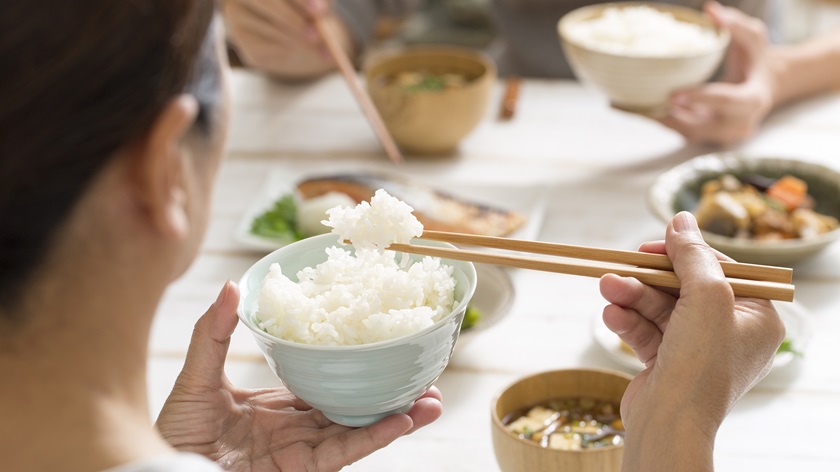 A woman eats rice from a bowl using chopsticks.