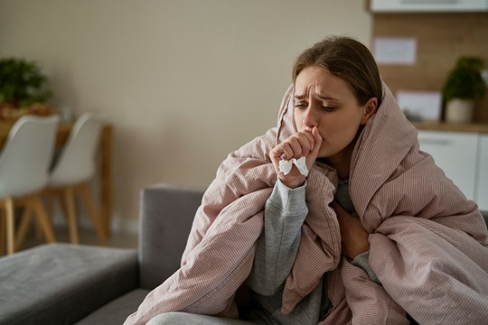 A woman with the ‘flu is coughing and is wrapped in a blanket.