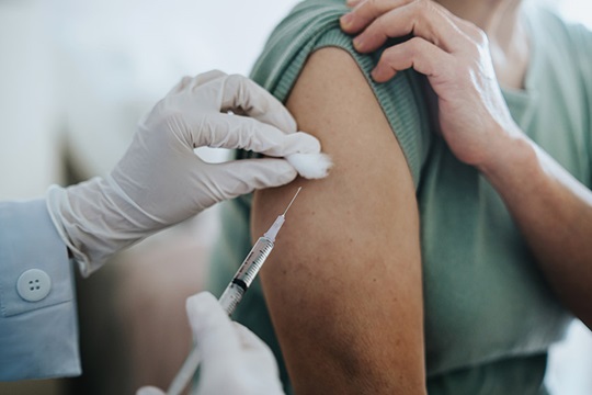 Close-up of an arm being injected with a vaccine using a needle and syringe.