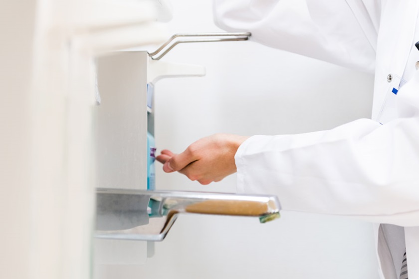 A doctor disinfects his hands at a disinfectant dispenser.