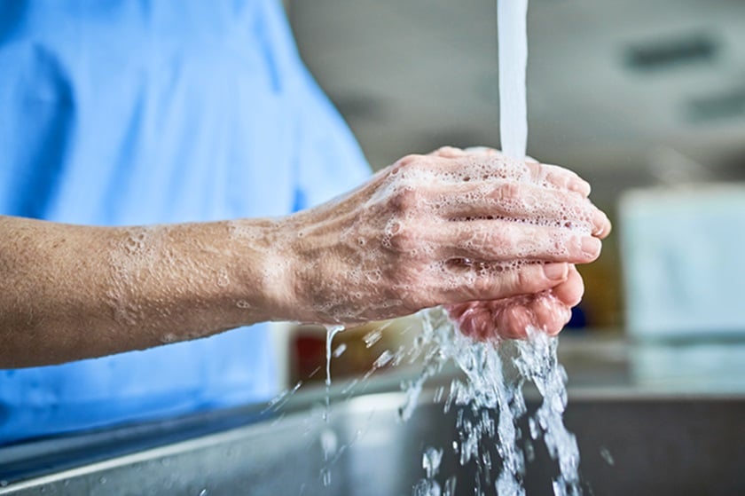 A caregiver washes his hands under running water.